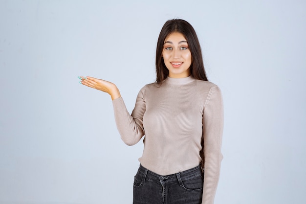 Foto gratuita ragazza in camicia grigia che mostra qualcosa in mano.