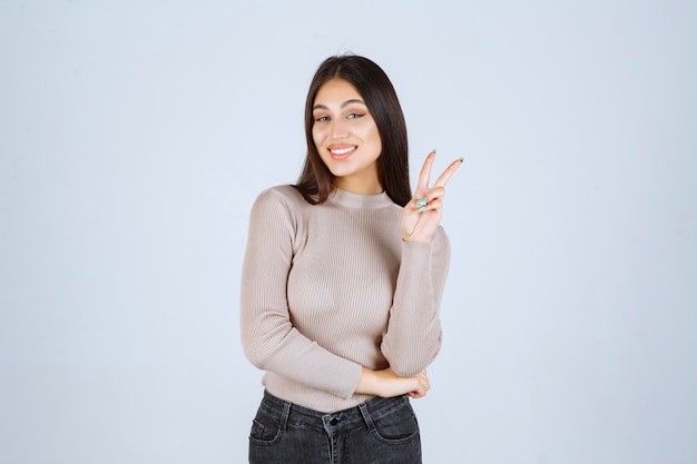 Girl in grey sweater doing peace hand sign.