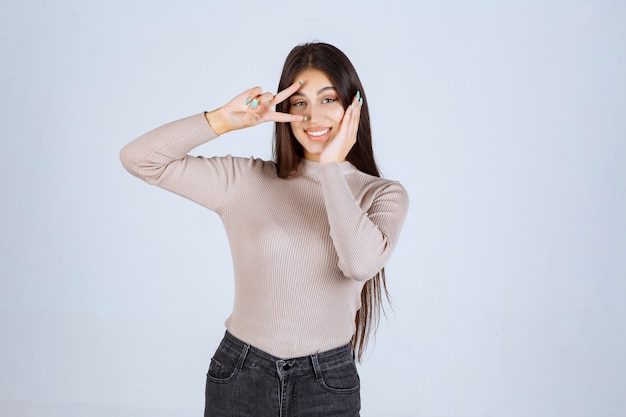 Girl in grey sweater doing peace hand sign.