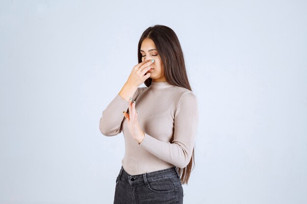 Girl in grey sweater feels bad smell and covering nose. 