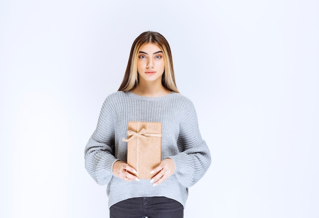 Girl in grey sweater holding a cardboard gift box.