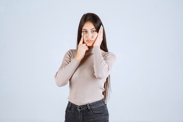 Girl in grey sweater holding her face and head. 