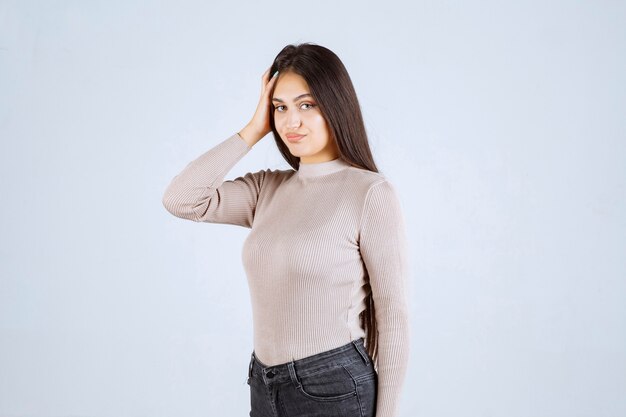 Girl in grey sweater holding her face and head. 