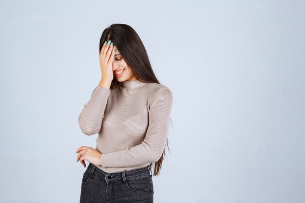 Girl in grey sweater holding her face and head.