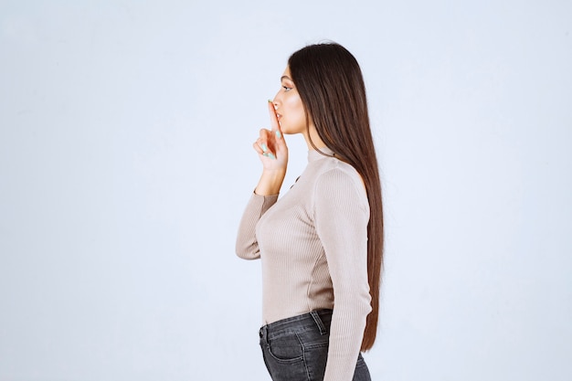 Ragazza in maglione grigio che fa segno silenzioso.