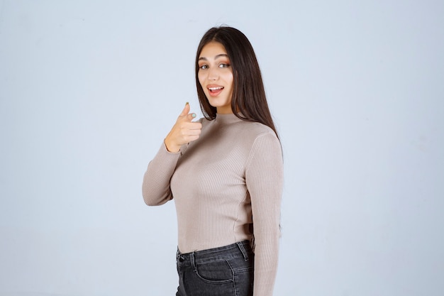 Girl in grey sweater making thumb up sign.