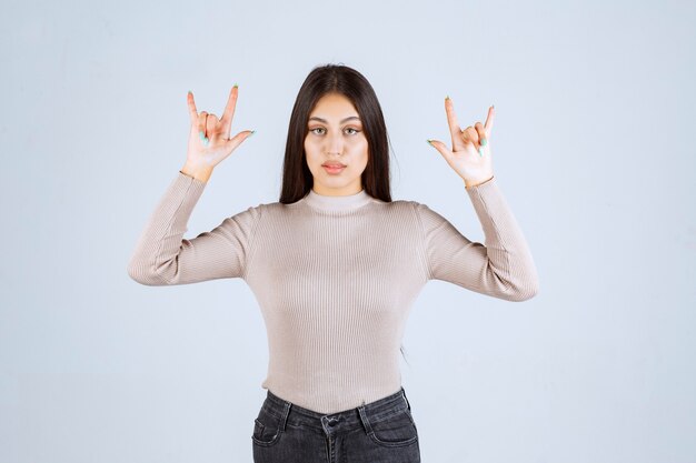 Girl in grey sweater making wolf sign. 