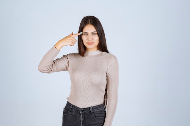 Girl in grey sweater pointing her head.