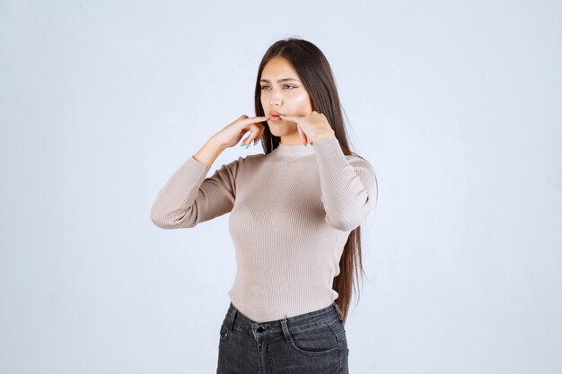 Girl in grey sweater putting fingers to her mouth and whistling. 