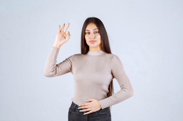 Девушка в сером свитере, показывая знак ОК круга.