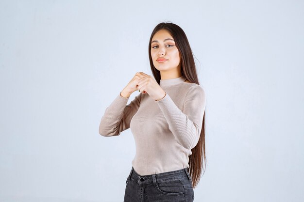 Девушка в сером свитере показывает кулаки и силу.
