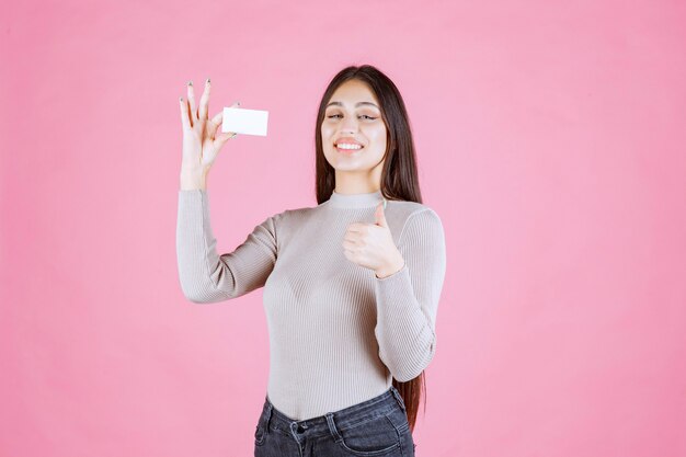 좋은 손 기호를 만드는 그녀의 새로운 명함을 보여주는 회색 스웨터에 소녀