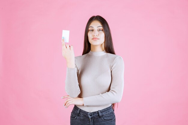 Foto gratuita ragazza in maglione grigio, mostrando e presentando il suo biglietto da visita