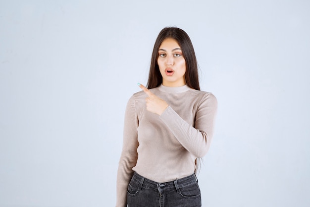 Girl in grey sweater showing something on the left. 