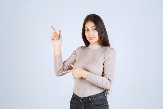 Girl in grey sweater showing something on the left. 