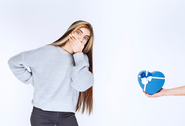 Free photo girl in grey sweatshirt getting surprized by the blue heart shape gift box.