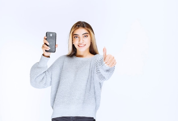 Girl in grey sweatshirt holding a black smartphone and feeling satisfied.