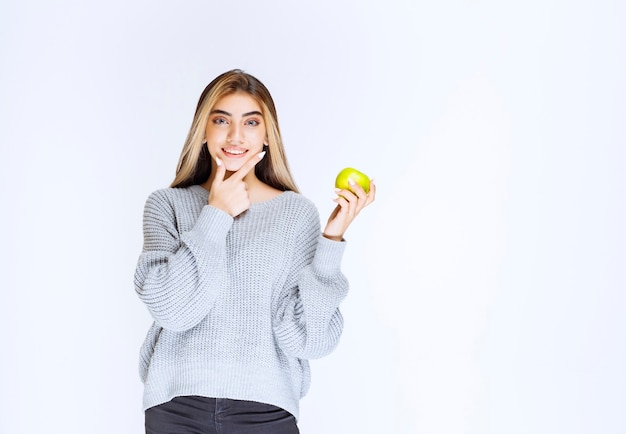 Girl in grey sweatshirt holding green apple in the hand.