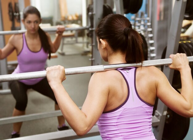 girl in the gym lifts the bar in front of the mirror