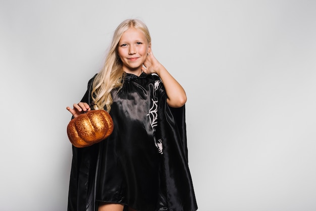 Girl in Halloween costume holding pumpkin