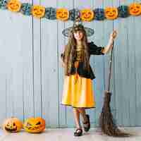 Free photo girl in halloween costume standing with broom and pumpkins