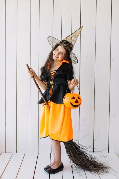 Free photo girl in halloween costume with pumpkin basket and broom posing in studio