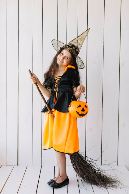 Девушка в костюме Хэллоуина с корзиной тыквы и метлой, которая позирует в студии