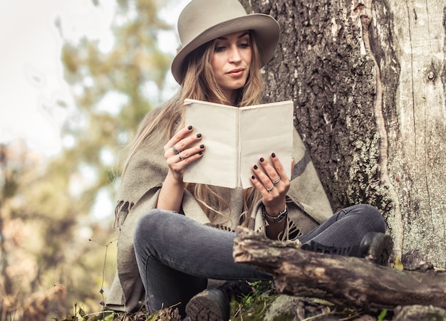 girl in a hat reading a book in autumn forest