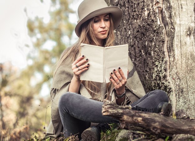 девушка в шляпе читает книгу в осеннем лесу
