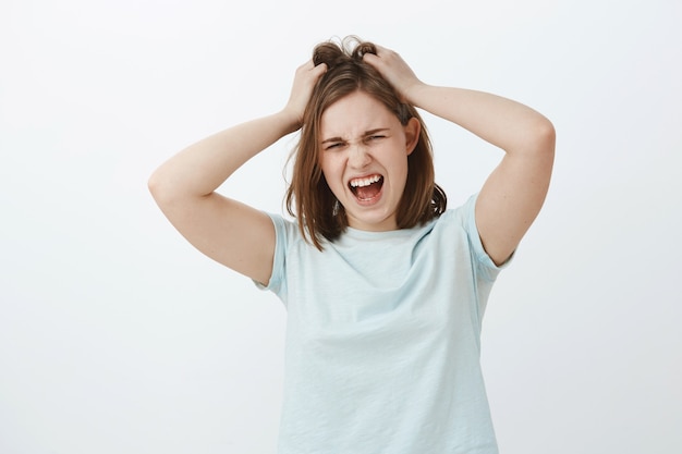 Girl hates think too much. Displeased distressed young upset european woman with brown short haircut screaming while losing temper being angry or mad messing up or pulling hair out of head