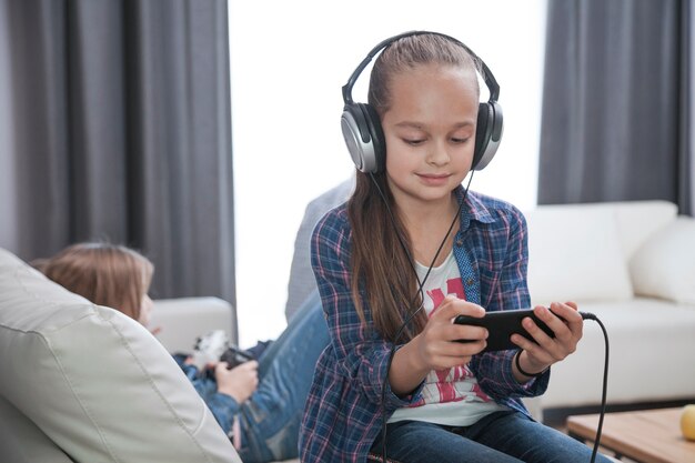 Girl in headphones using smartphone on sofa