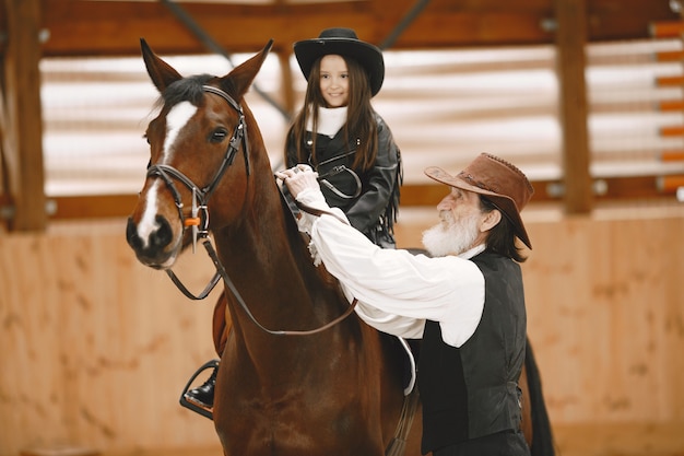 Foto gratuita ragazza in casco imparare a cavallo. l'istruttore insegna alla bambina.