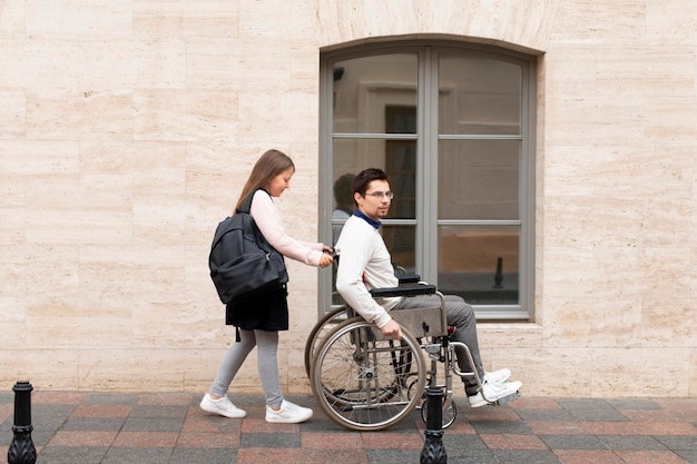 Foto gratuita ragazza che aiuta un disabile che viaggia in città