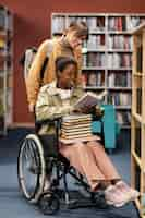 Free photo girl helping her colleague in wheelchair choose a book for a project