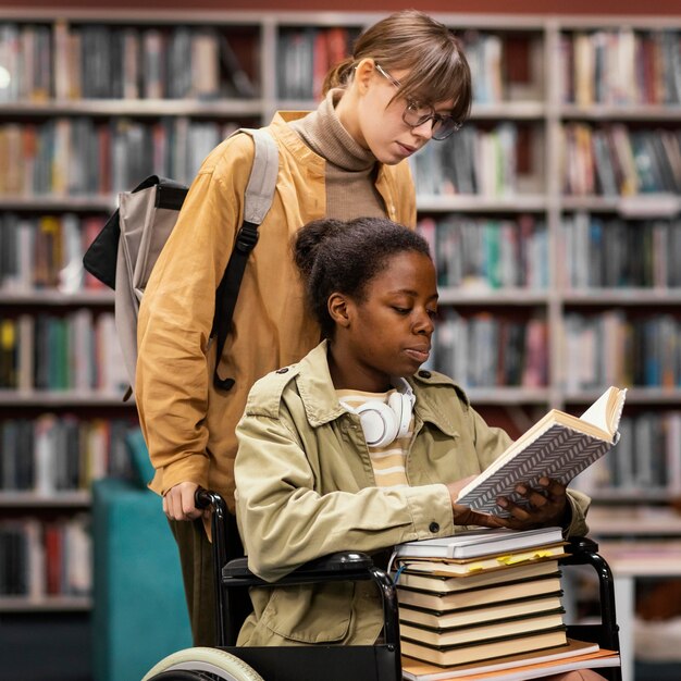Girl helping her colleague in wheelchair choose a book for a project