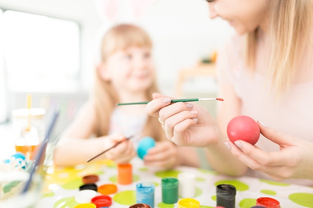 Girl helping mother to paint eggs