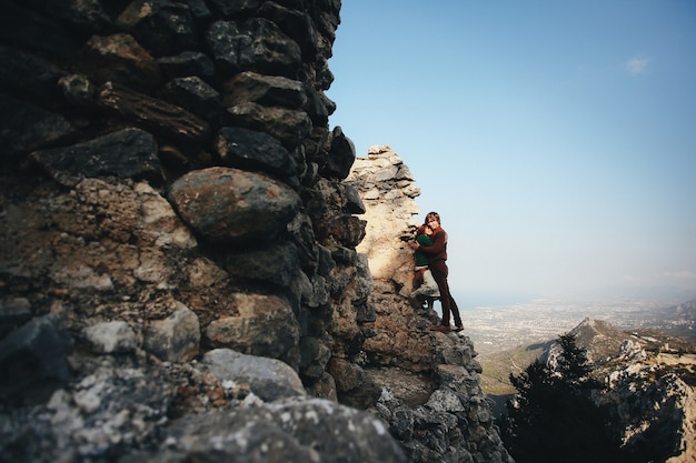 Girl and her boyfriend are hugging leaning to the rock on the landscape