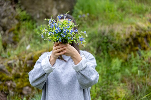 소녀는 숲에서 수집 한 신선한 꽃 꽃다발 뒤에 얼굴을 숨 깁니다.