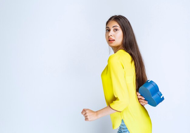 Girl hiding the blue heart shape gift box behind herself.