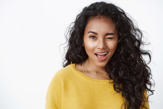 Foto gratuita ragazza che suggerisce che fa la prima mossa carina donna dai capelli ricci afro-americana impertinente in maglione giallo che fa l'occhiolino civettuola e sorridente incoraggiare l'amico tutto bene in piedi sfondo bianco positivo