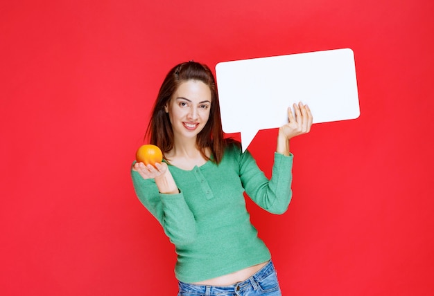 Девушка держит свежий апельсин и доску информации прямоугольника.