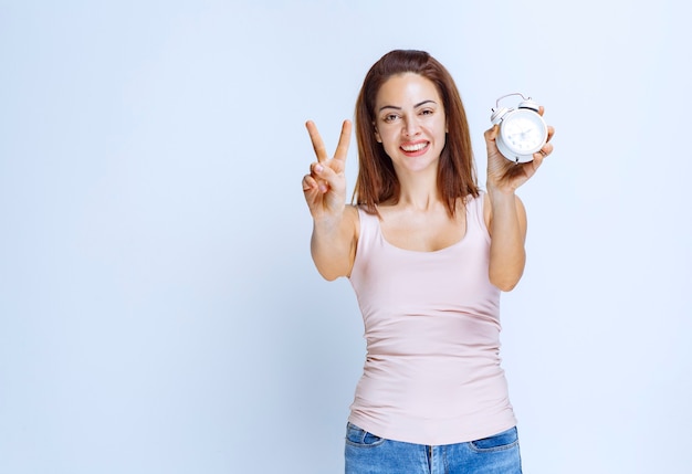 Girl holding an alarm clock and pointing at it. 