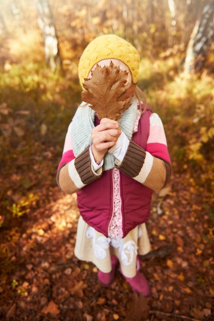 Girl holding autumn leaf on her face