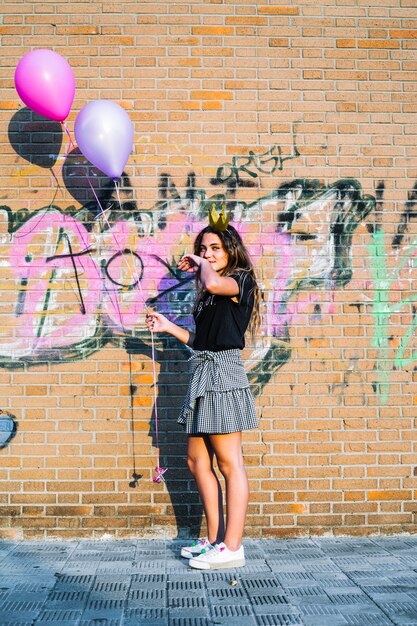 Girl holding balloons in front of graffiti wall