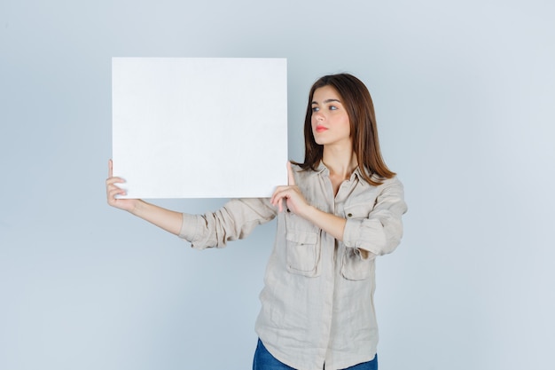 girl holding blank canvas in shirt and looking focused