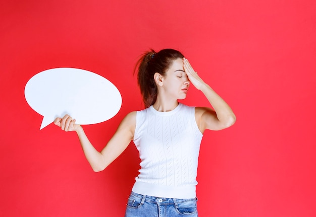 Free photo girl holding a blank ovale ideaboard for gaming and looks exhausted.