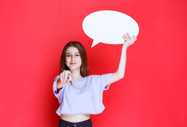 Girl holding a blank ovale info board and pointing at something. 