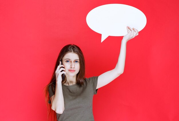 Girl holding a blank ovale info board and talking to the phone. 