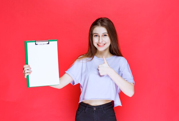 Free photo girl holding a blank reporting sheet and showing enjoyment sign.