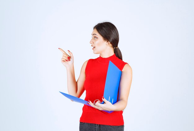 Girl holding a blue folder and pointing to the left.